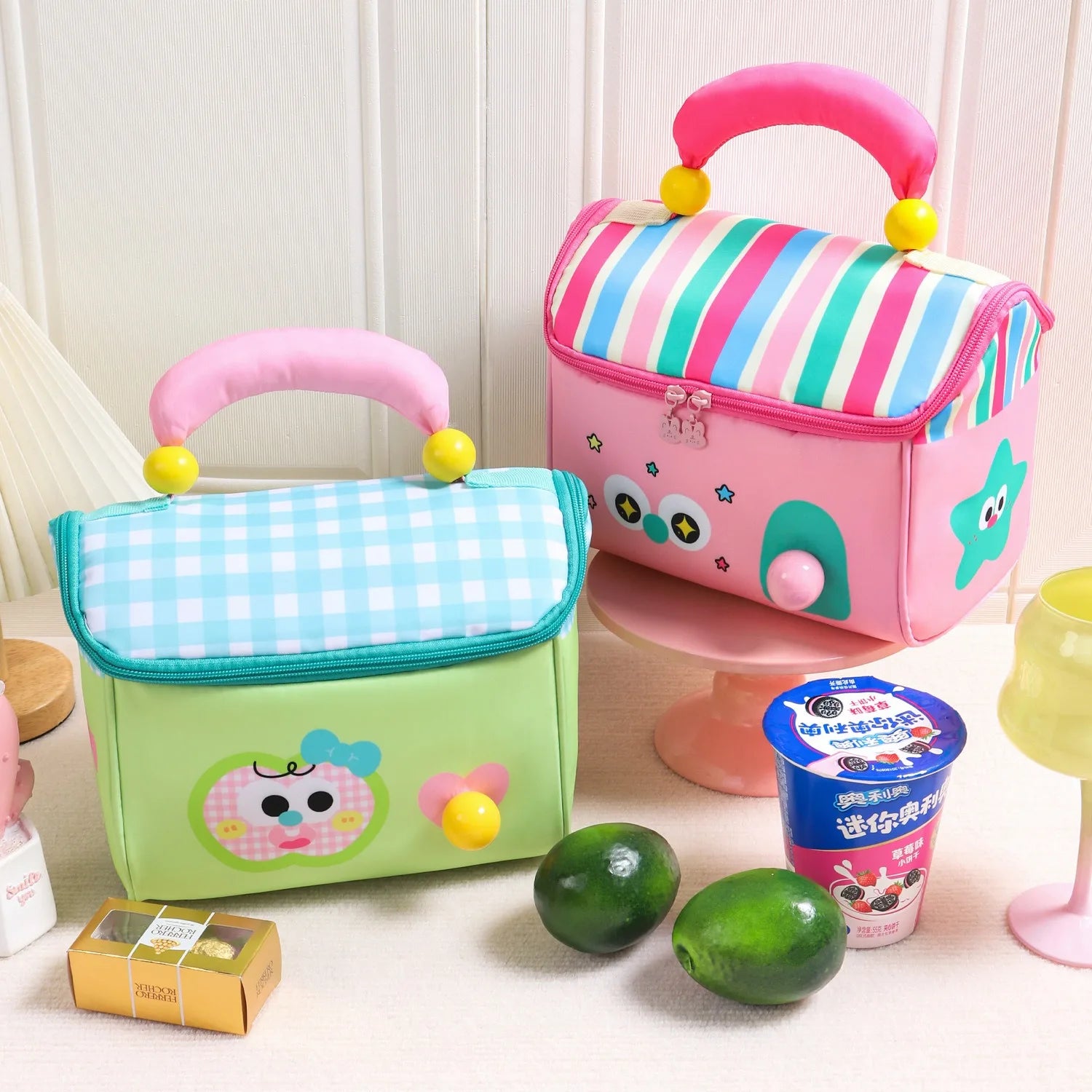 Two colorful children's kawaii lunch bags on a white surface with snacks and a cup.