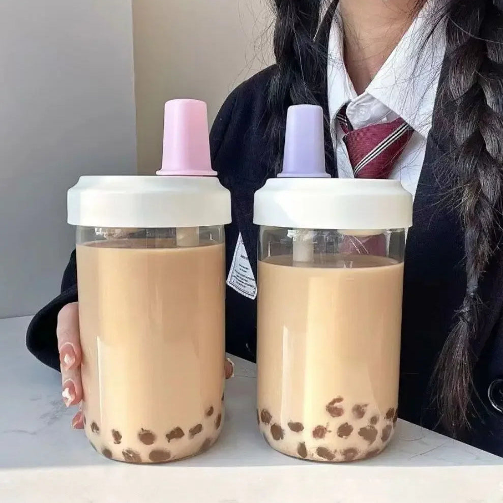 Two kawaii water bottles of bubble tea with different colored lids held by a person.