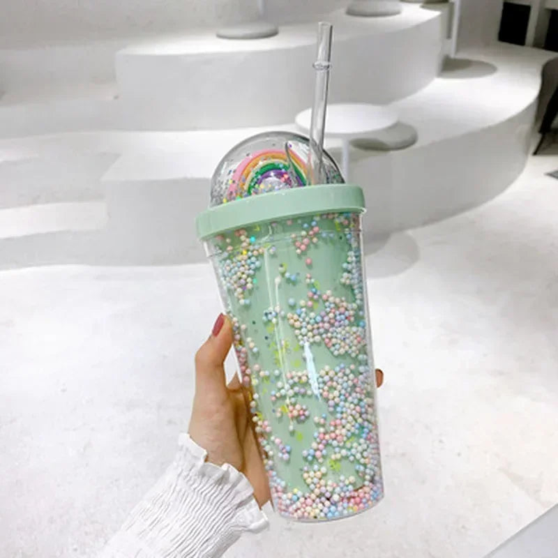 Hand holding a mint green kawaii tumbler with a rainbow design and colorful beads against a white background.