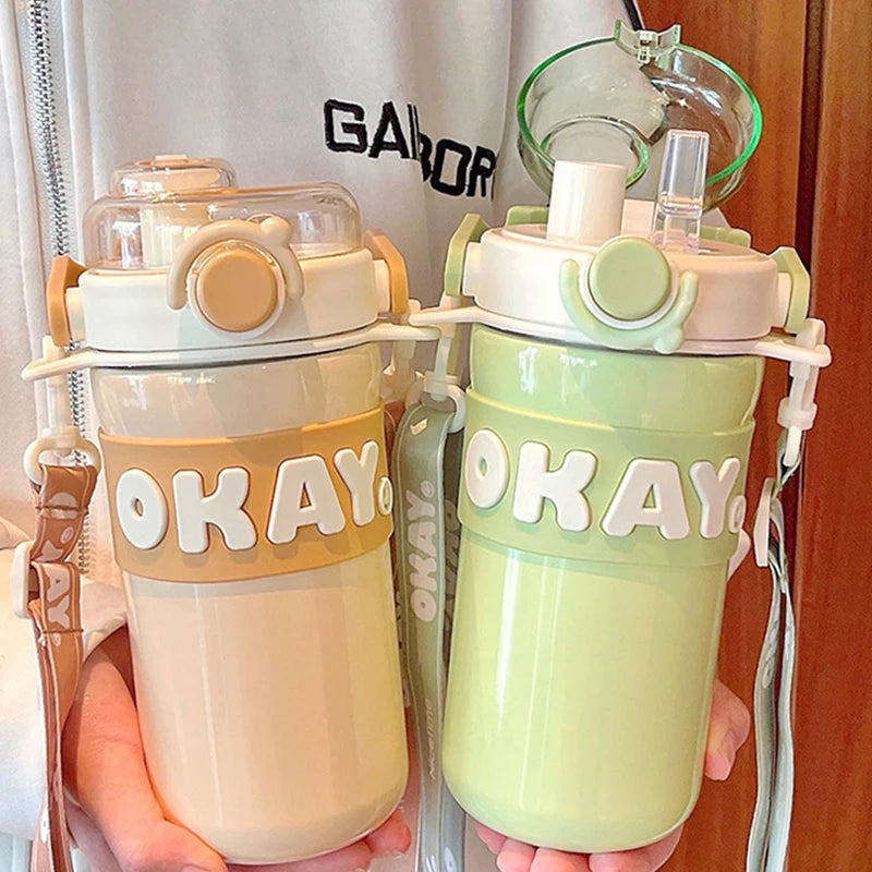 Two kawaii water bottles with 'OKAY' text held by a person wearing a Gabor shirt.