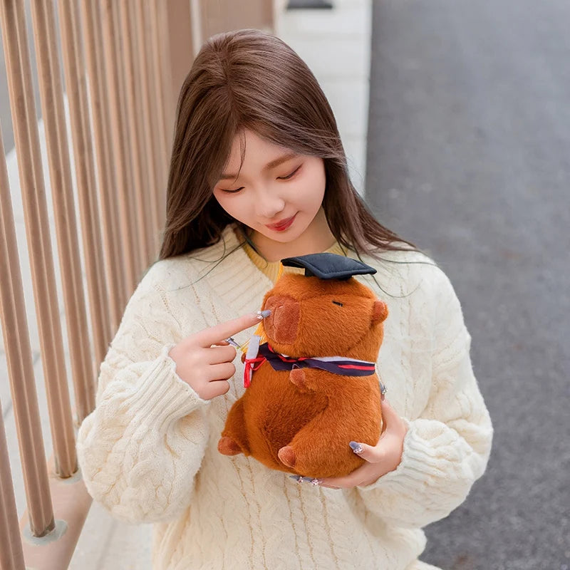 Woman holding a capybara plush toy resembling a bear with a graduation cap and gown.