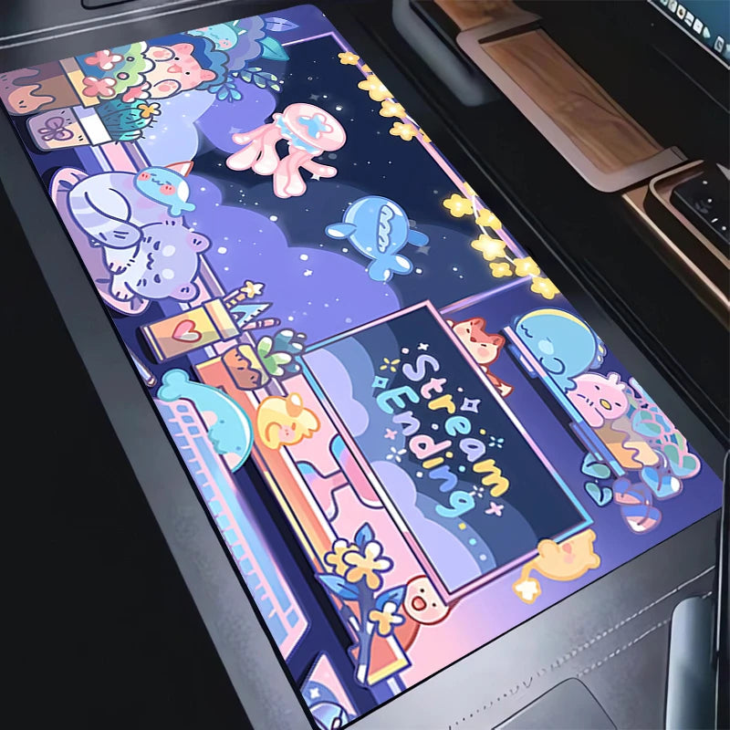 A rectangular desk mat with a colorful cartoon space-themed design, shown laid out on a dark desk next to a laptop. The mat features cute characters, planets, stars, and the text 'Space Jamming'.
