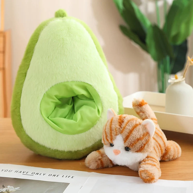 Avocado-shaped kawaii plush toy and a small cat plush toy on a wooden surface with a plant in the background.