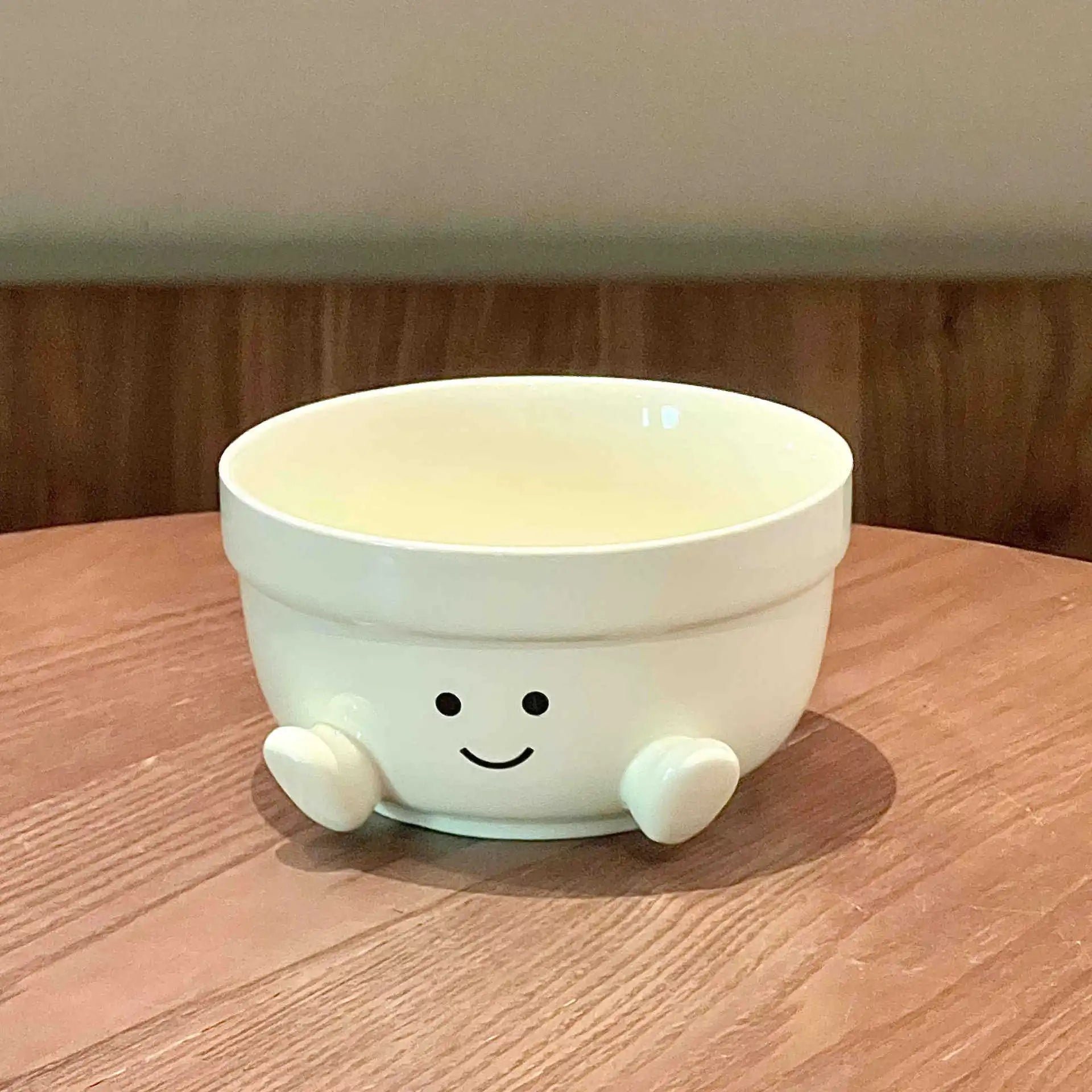 White ceramic kawaii bowl with a smiley face and legs on a wooden surface