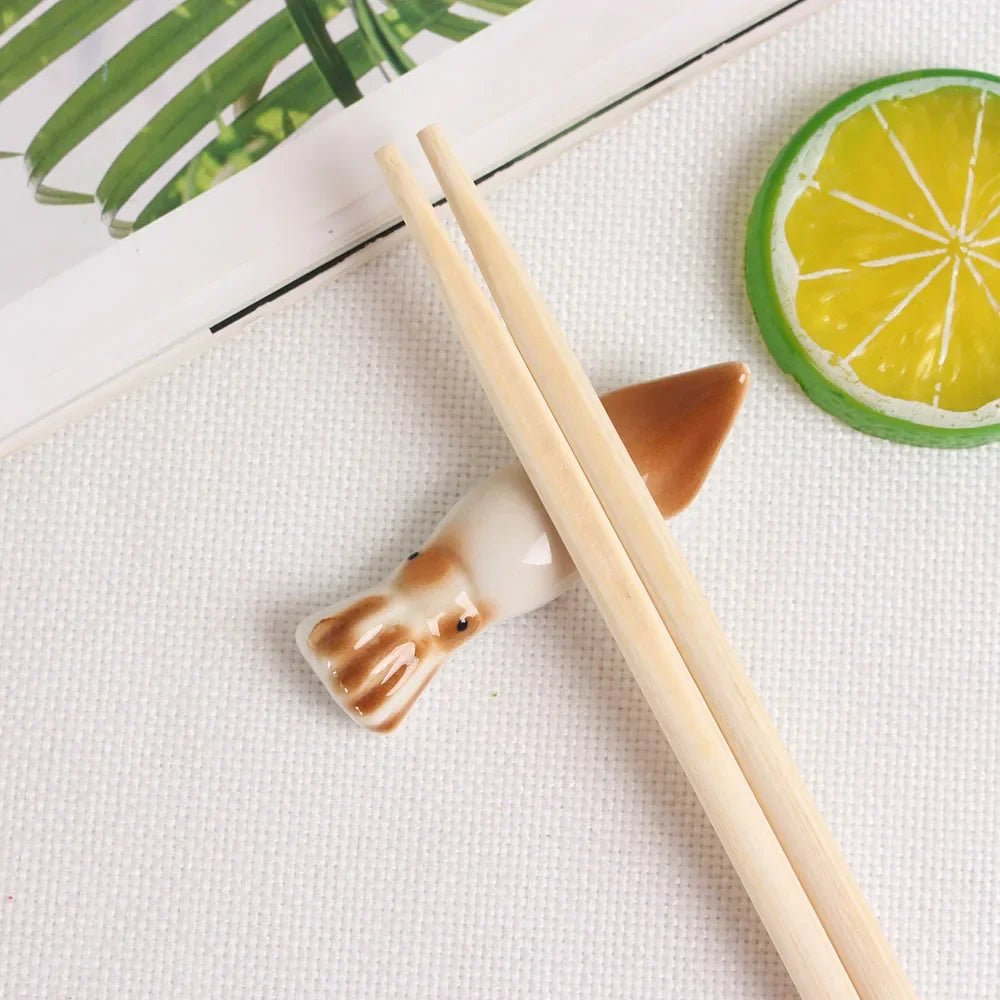 Chopsticks with a cat-shaped kawaii chopstick holders on a white surface with a lemon slice and green leaves.