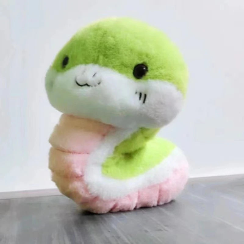 Plush kawaii toy snake with green head and pink body on a gray surface