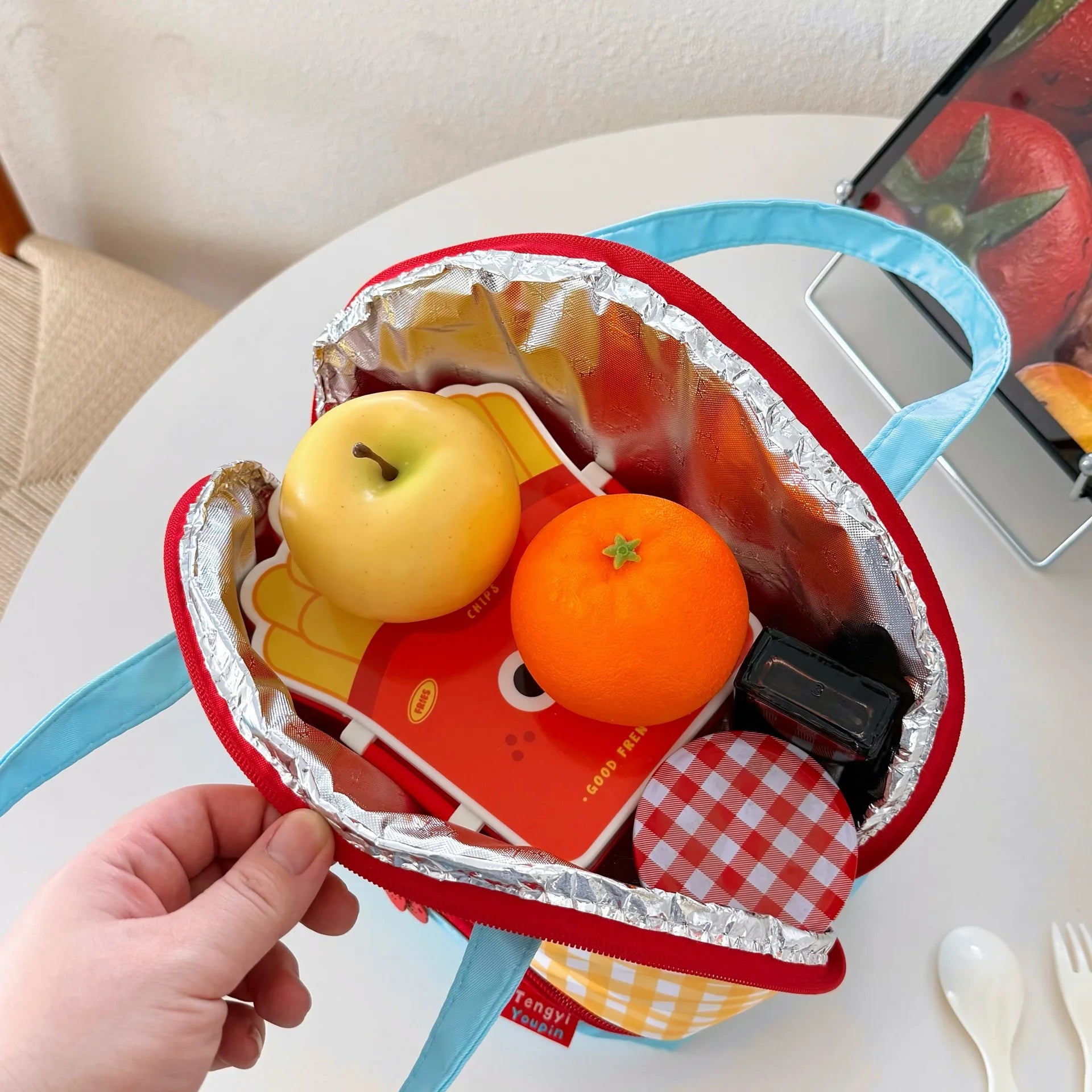 Heart-shaped kawaii lunch bag with apples, oranges, and a sandwich on a white surface.