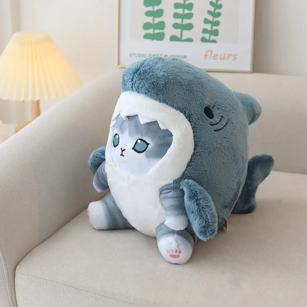 Plush kawaii toy shark on a couch with a lamp and wall art in the background