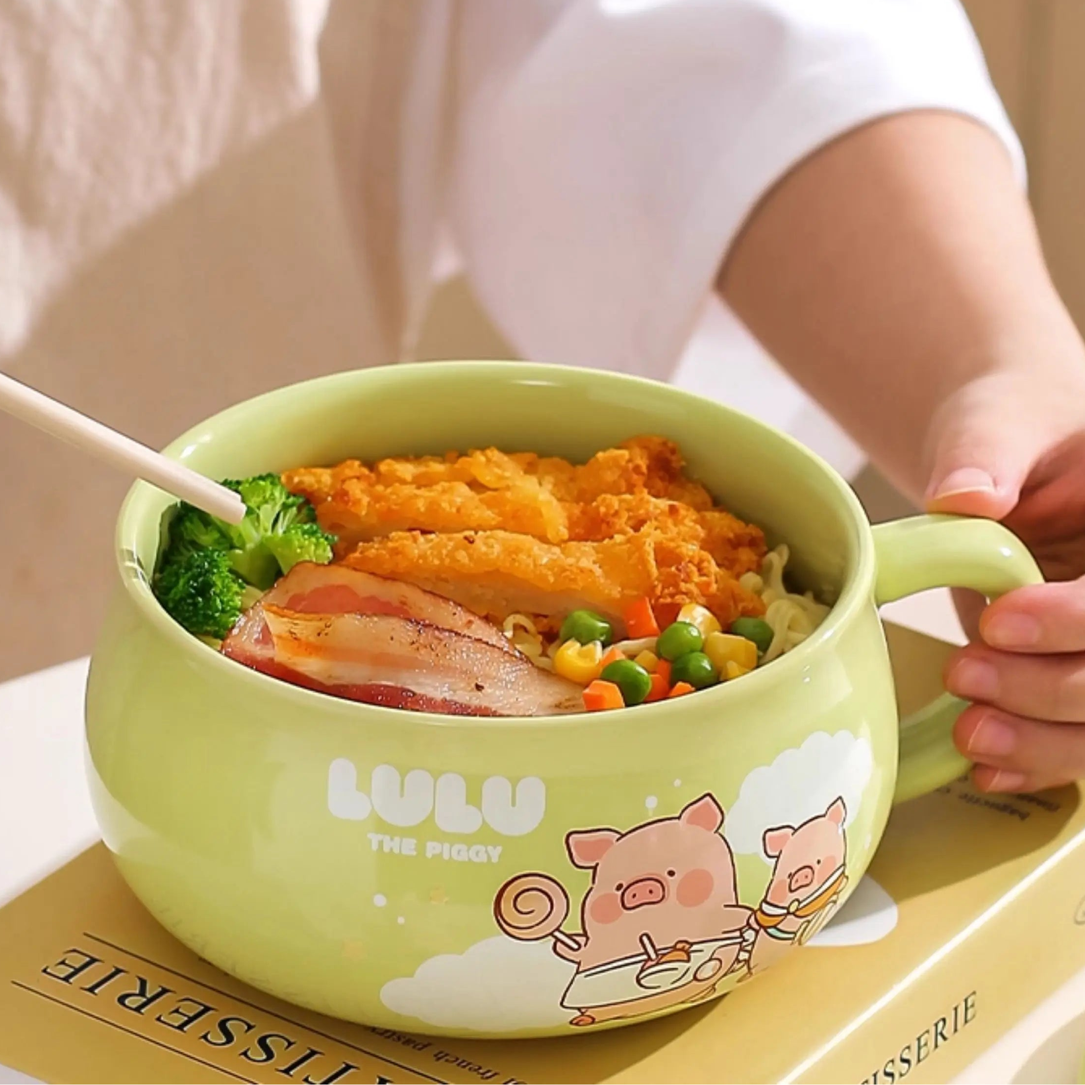 Green children's kawaii ramen bowl with cartoon design filled with food, held by a person.