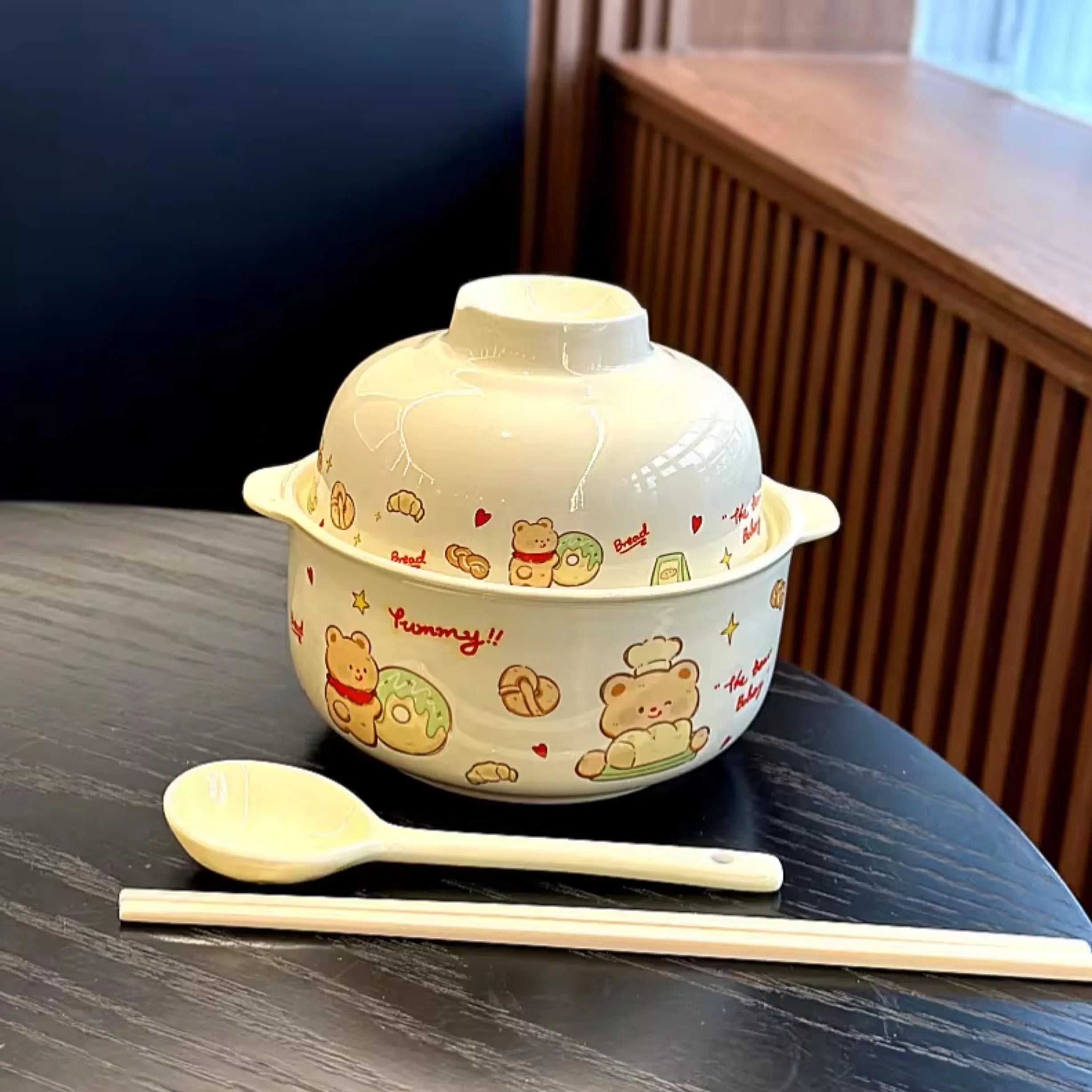 Ceramic kawaii ramen bowl with lid, spoon, and chopsticks on a dark surface