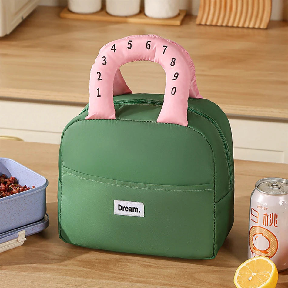 Green kawaii lunch bag with a pink handle featuring numbers on a wooden surface.