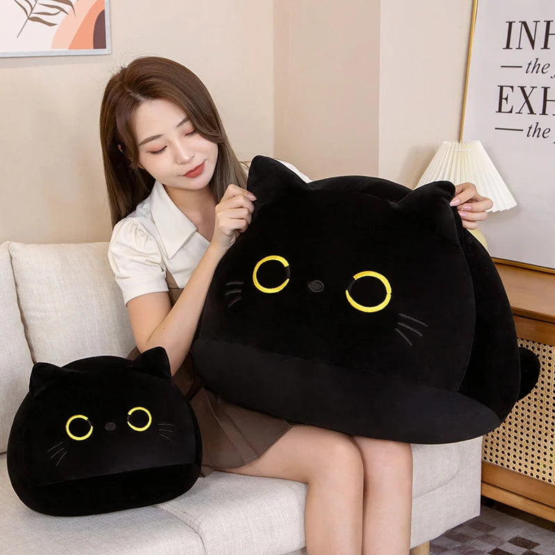 Woman holding a large black cat-shaped kawaii pillow with yellow eyes on a couch.
