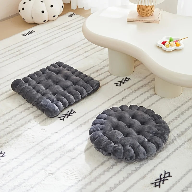 Two gray textured kawaii cushions on a white floor with a small table and decorative items in the background.