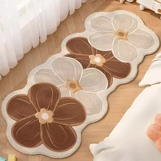 A long, cloud-shaped runner rug with a retro floral pattern, shown on a light wood floor next to a bed with white bedding.