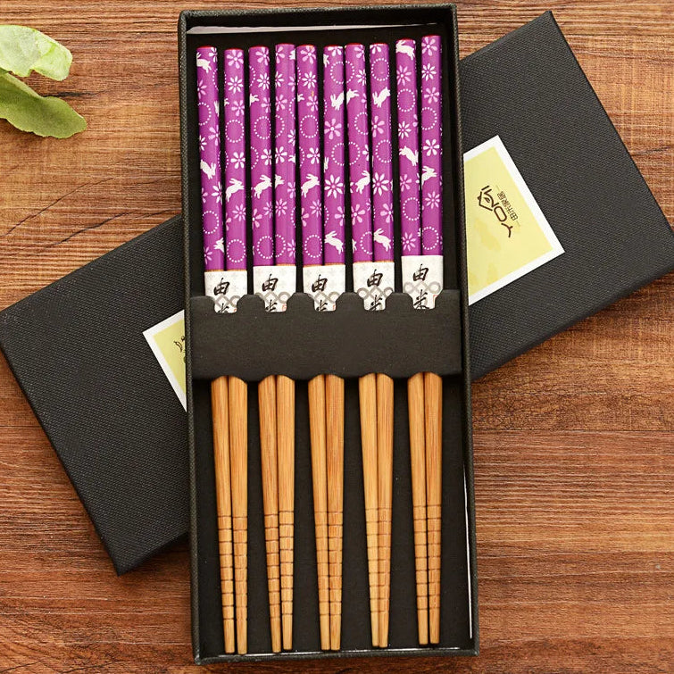 Set of wooden and purple patterned kawaii chopsticks in a black box on a wooden surface.