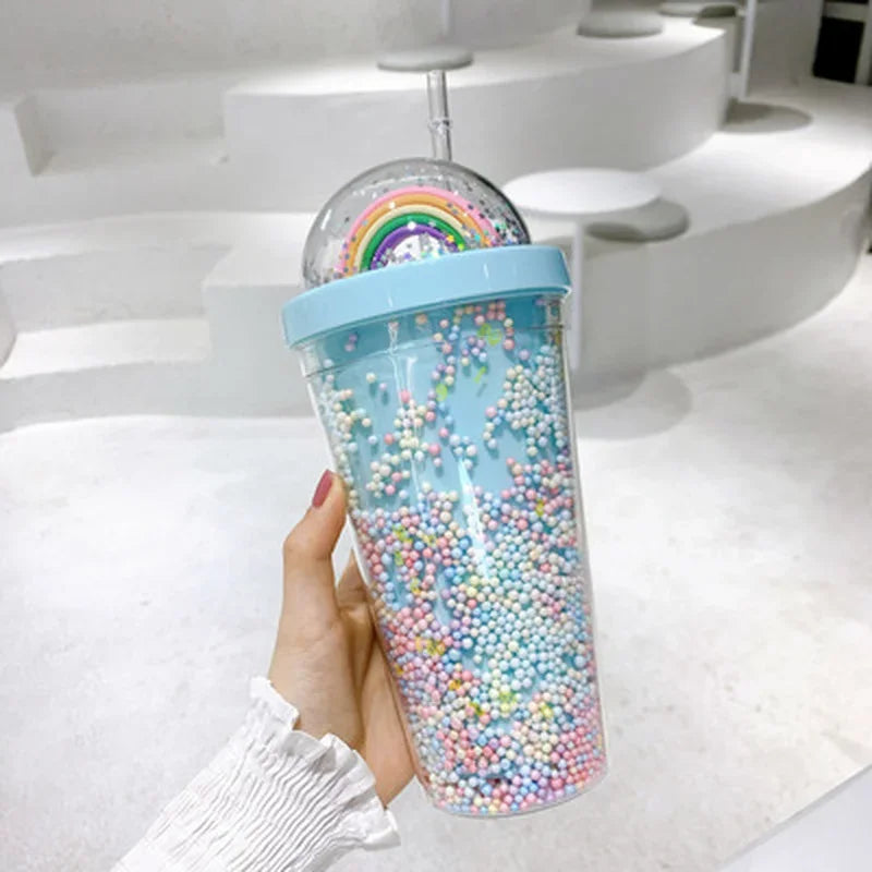Kawaii tumbler with colorful beads and a rainbow design held by a hand on a white surface.