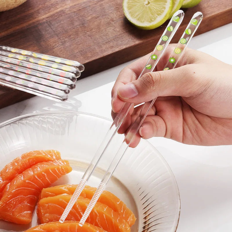 Clear kawaii chopsticks with green and red patterns being held over a plate of sushi.