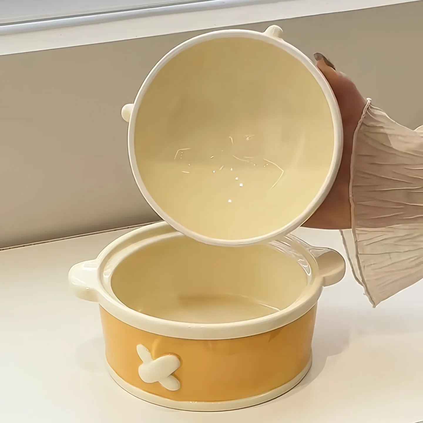 Yellow and white ceramic kawaii ramen bowl with lid held by a hand on a light background