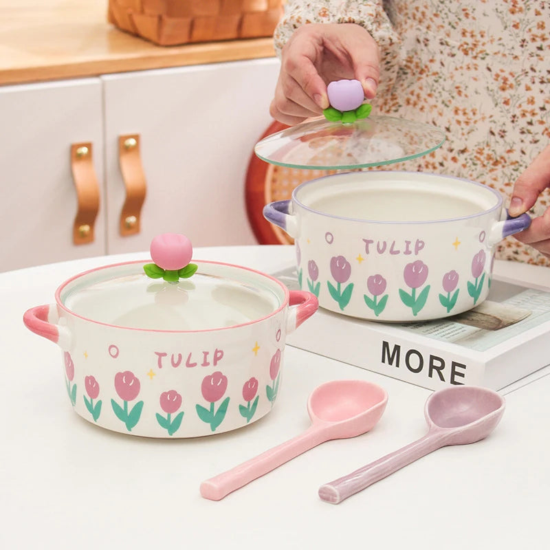 Ceramic kawaii ramen bowls with tulip design, pink spoons, and a hand holding a small pink object on a kitchen counter.