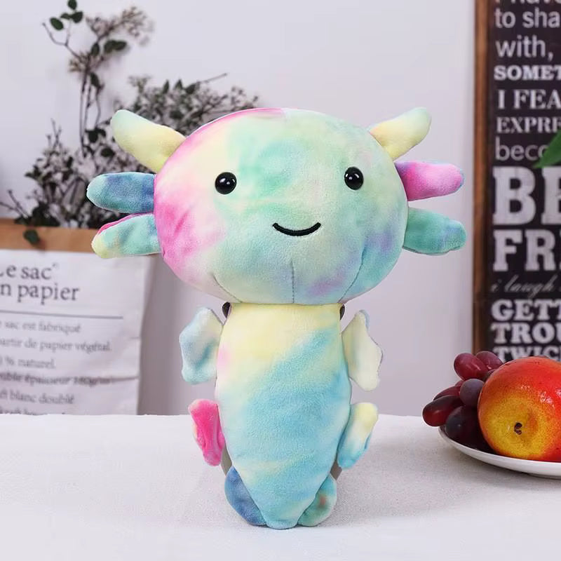 Colorful axolotl plush toy on a white surface with fruits and a plant in the background.