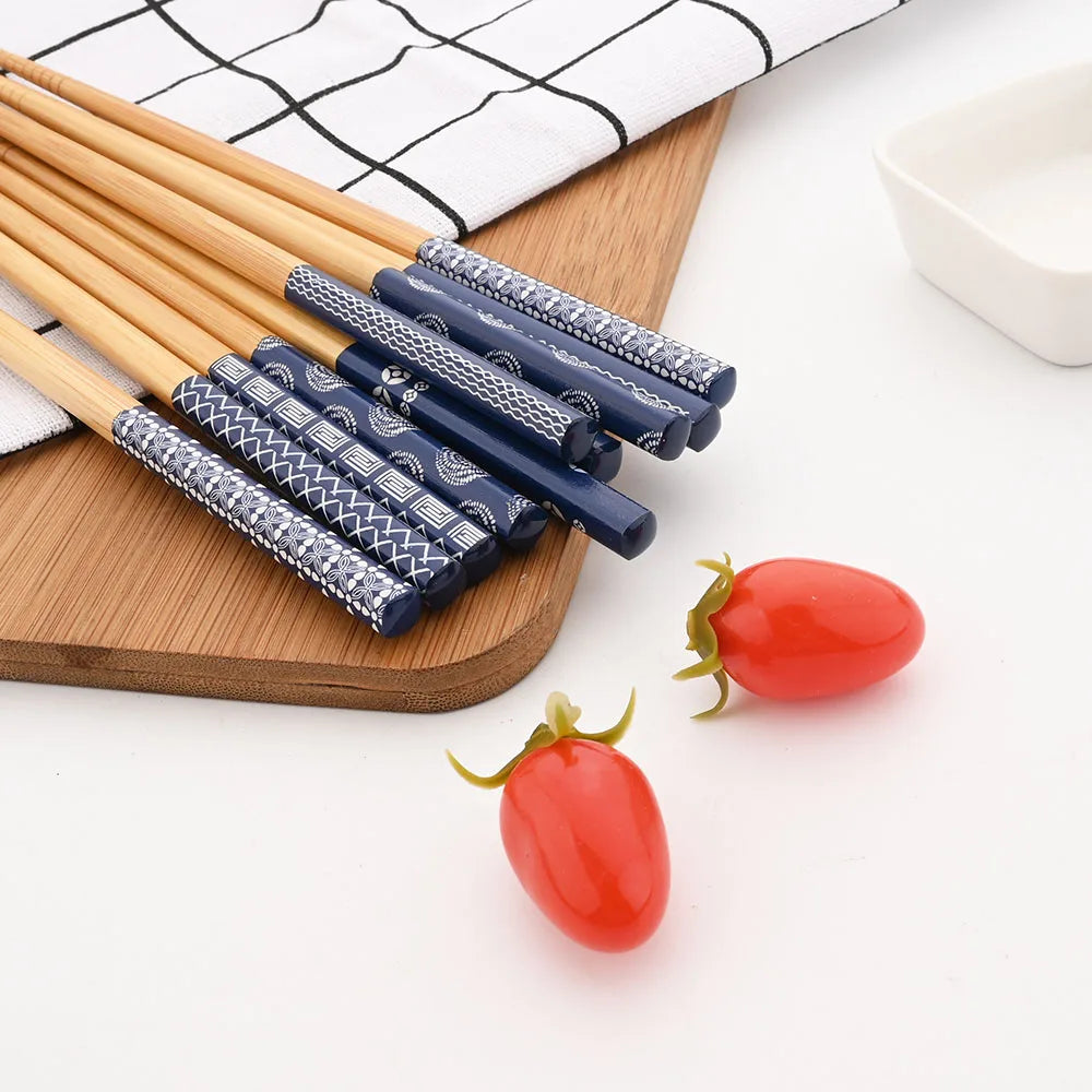 Set of blue and silver patterned kawaii chopsticks on a wooden board with red tomato-shaped objects.