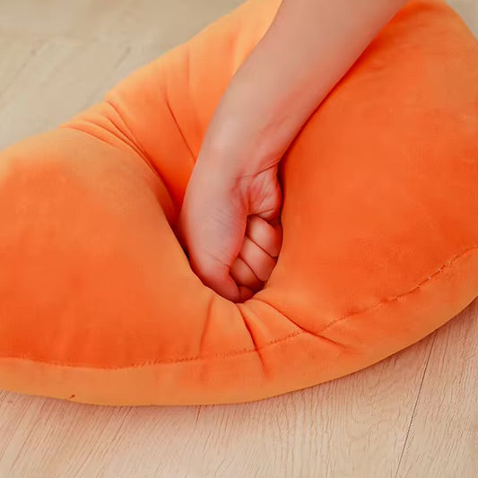 Carrot-shaped kawaii pillow with a hand resting on it on a wooden surface