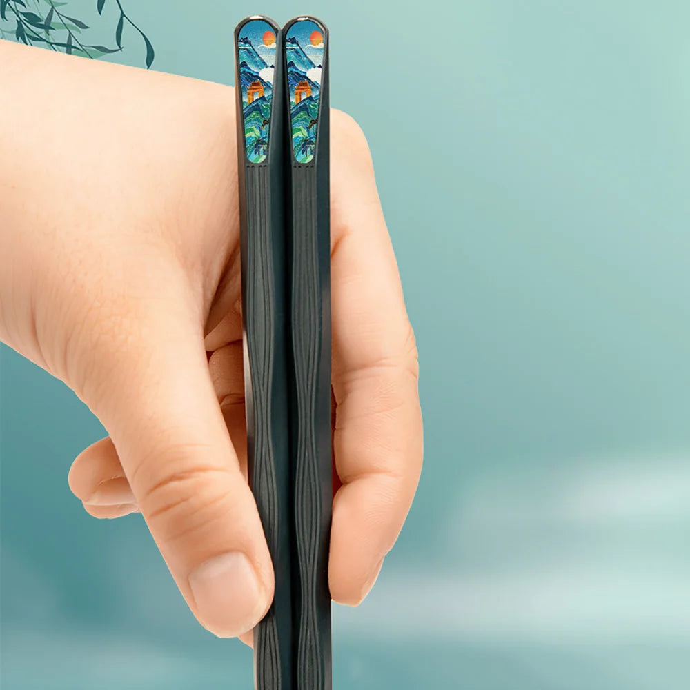 Hand holding a pair of black chopsticks with kawaii artistic ends against a light blue background