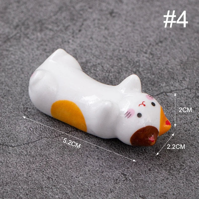 Small cat-shaped kawaii chopstick holders with measurements on a gray surface