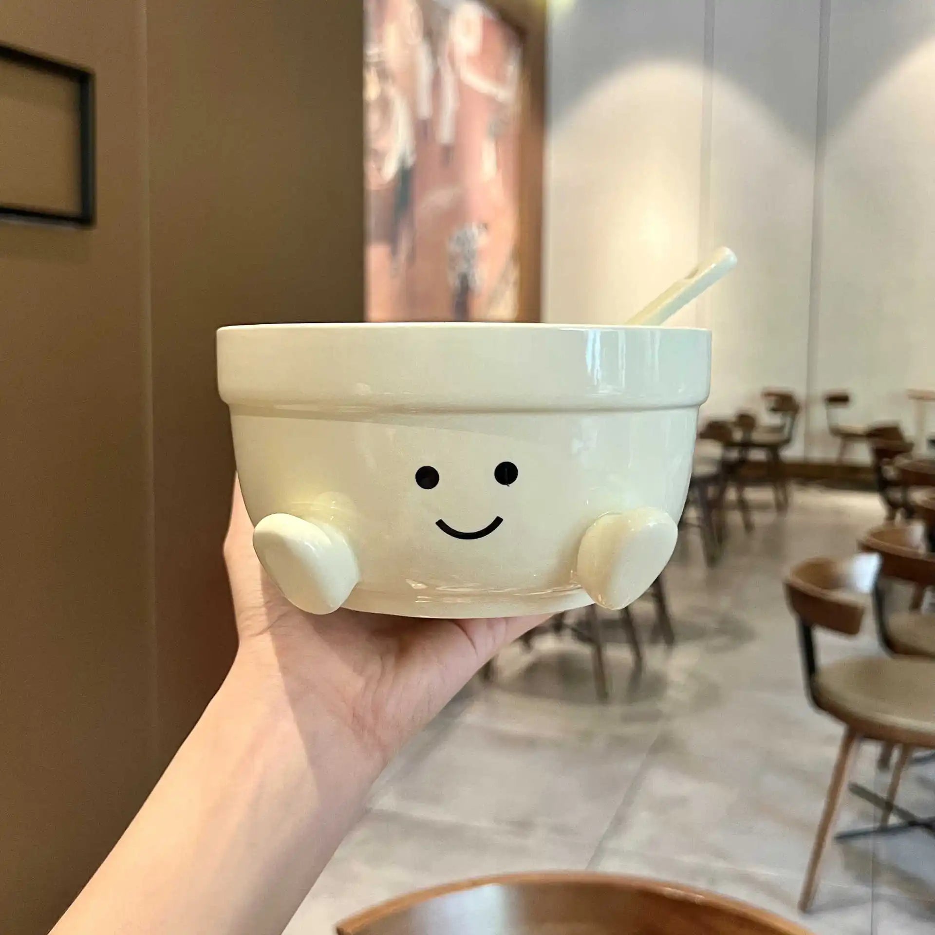 Person holding a white kawaii bowl with a smiley face design in a restaurant setting