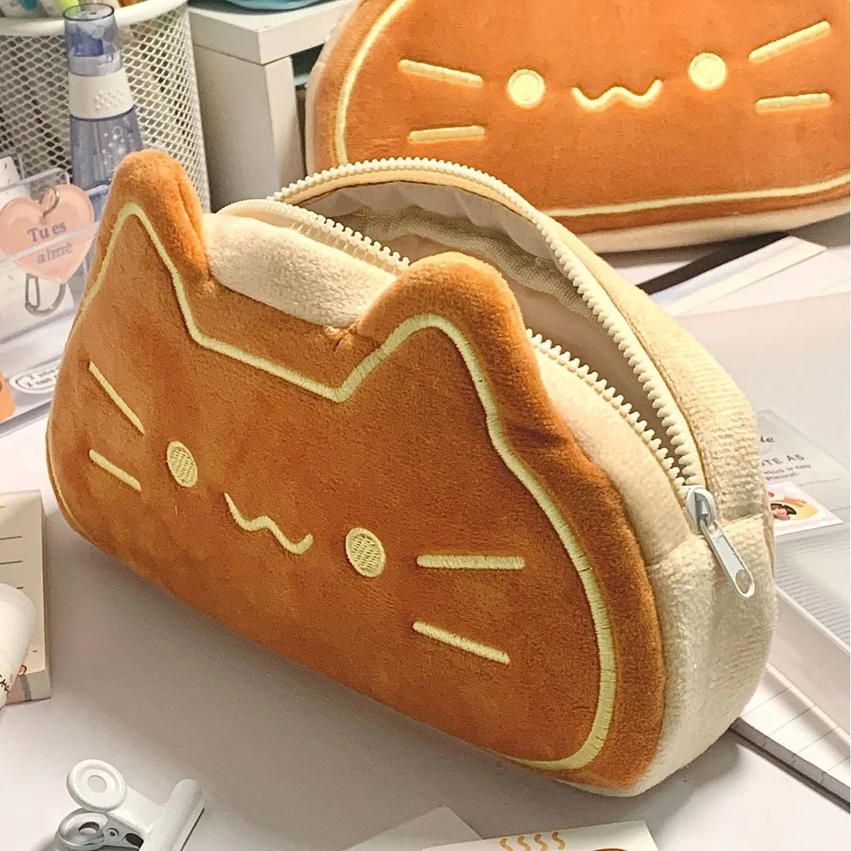 Cat-shaped plush kawaii pencil case on a desk with a water bottle and books in the background