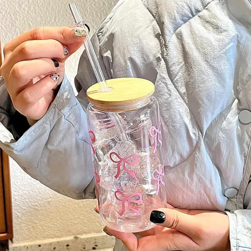 Clear kawaii tumbler with pink bows and a wooden lid held by a person wearing a light blue jacket.