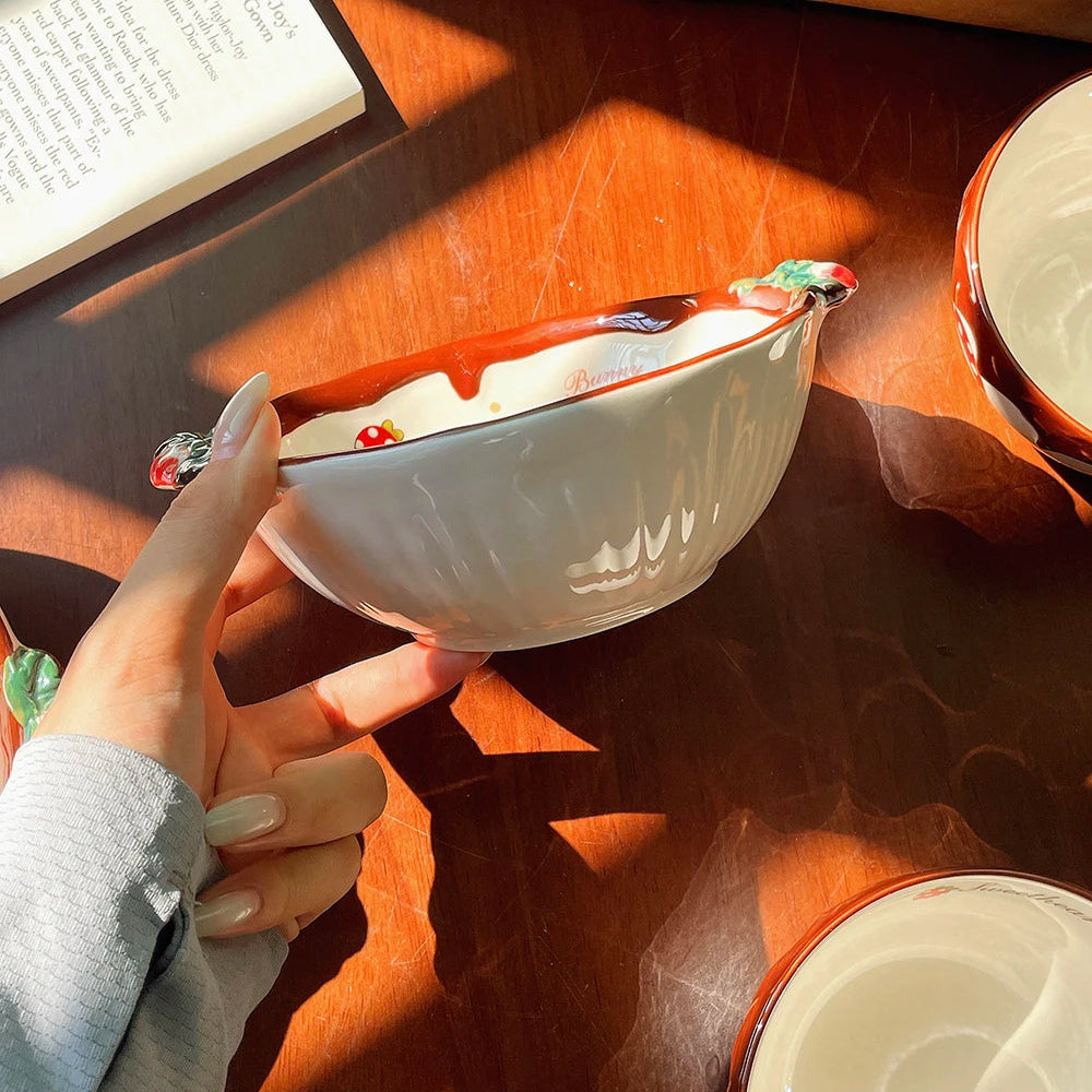 Person holding a white ceramic kawaii ramen bowl with red interior on a wooden table.