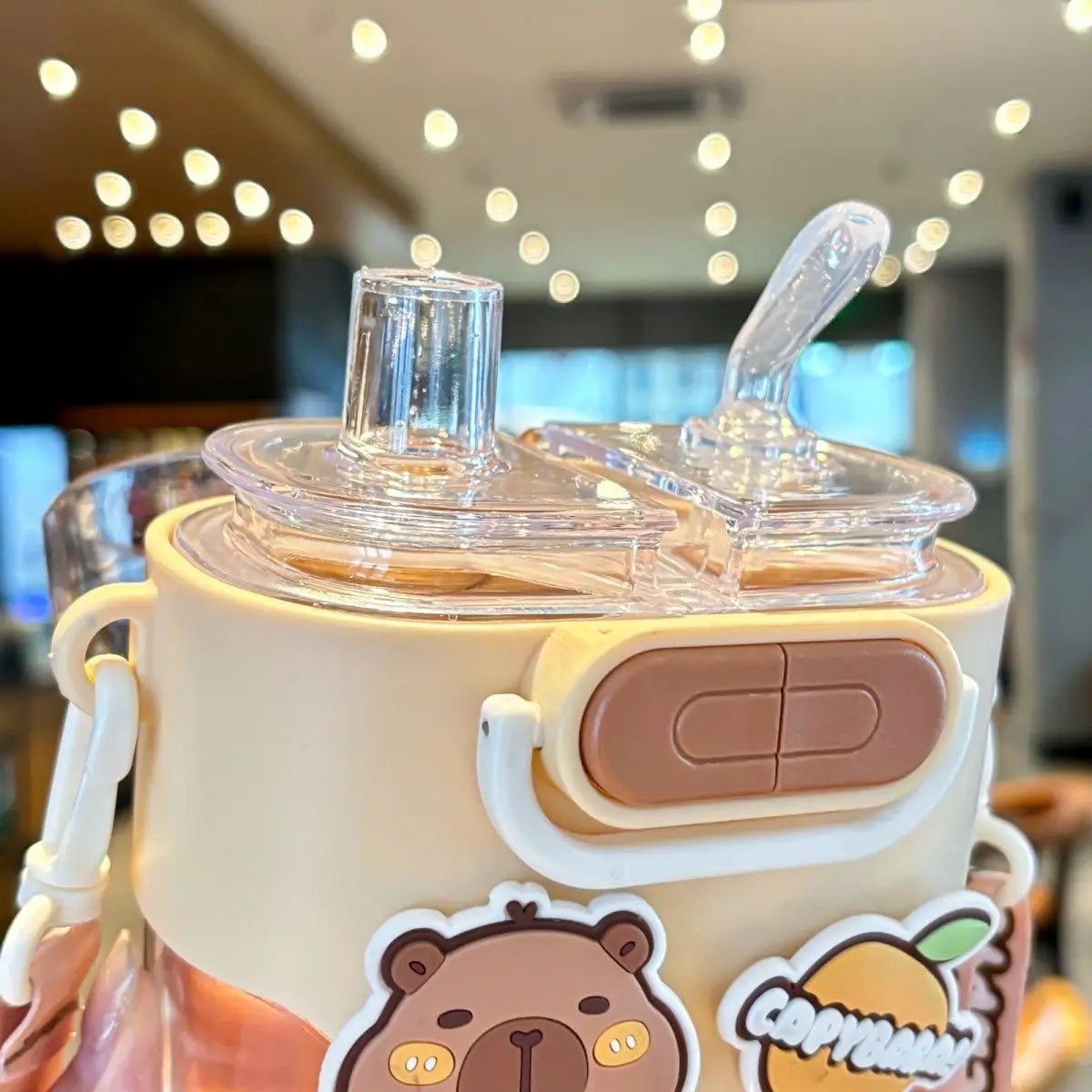 Children's kawaii water bottle with bear design and straw attachment in a blurred indoor setting