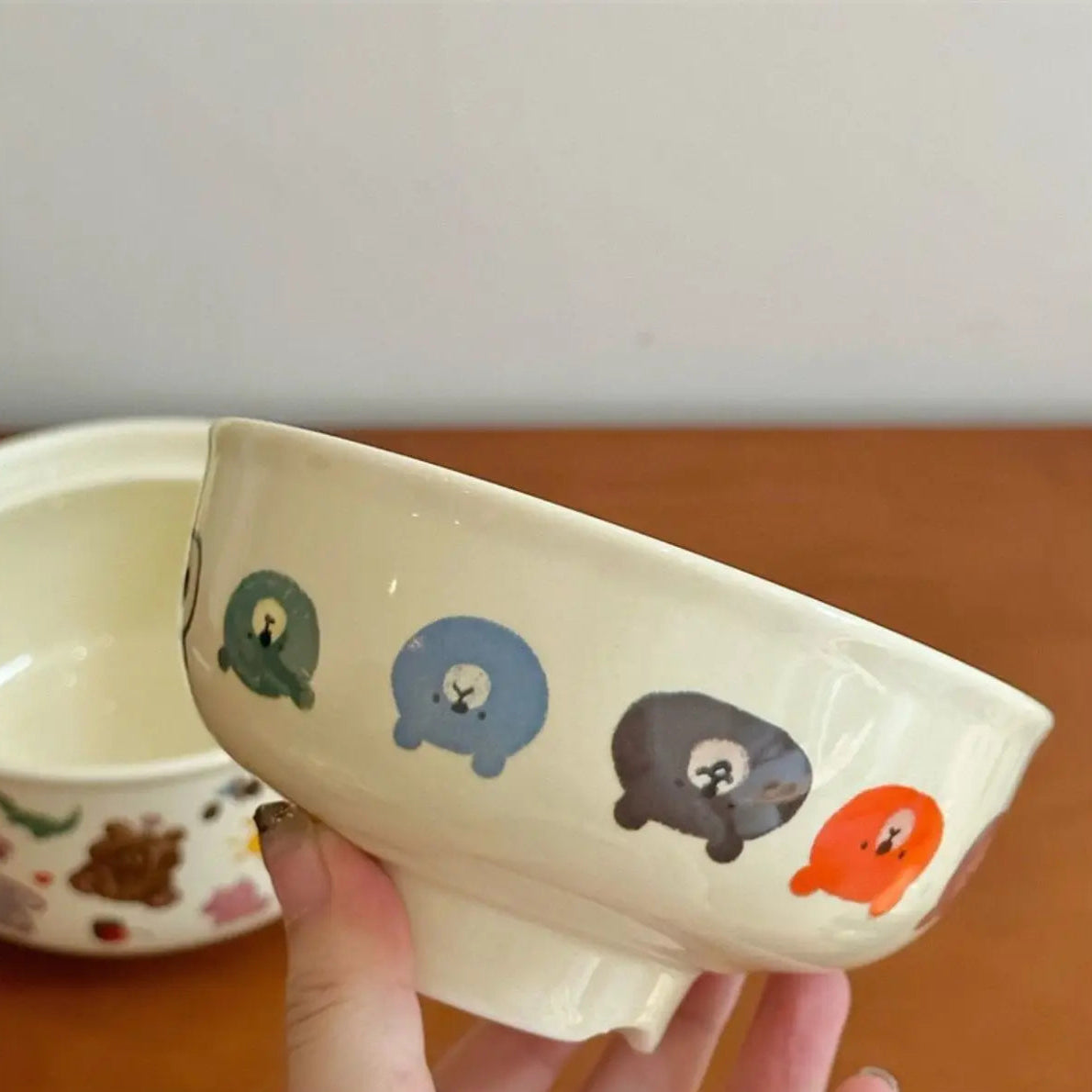 White ceramic kawaii bowl with cartoon animal designs held by a hand on a wooden surface.