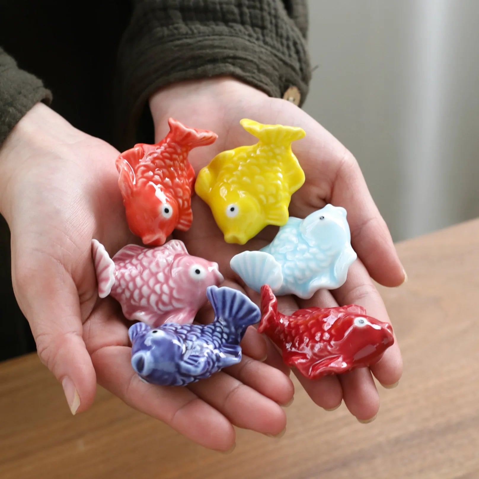 Colorful fish-shaped kawaii chopstick holders held in hands on a wooden surface