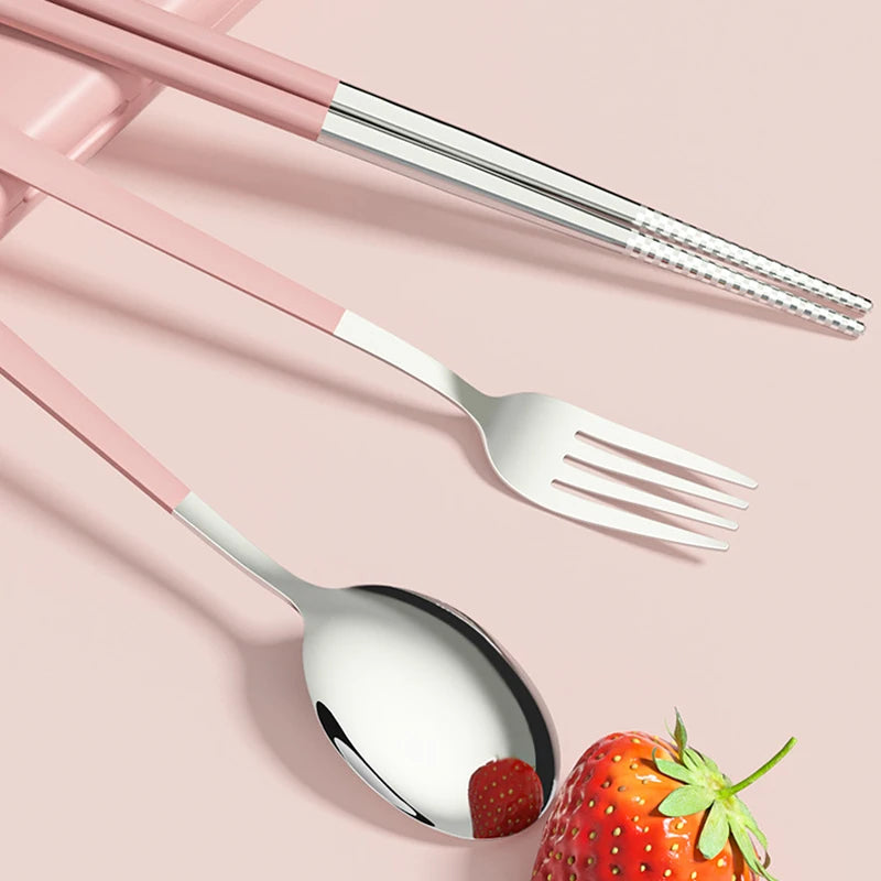 Silver kawaii utensils with pink handles on a pink background, accompanied by a strawberry.