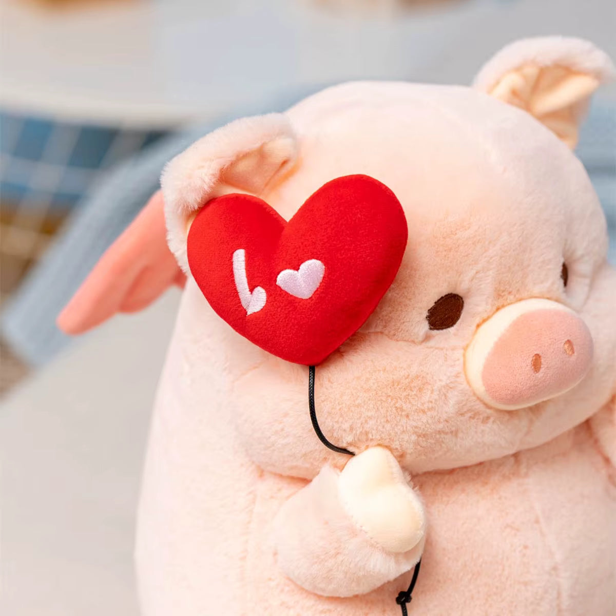 Plush pig toy with a red heart shaped 'I love you' sign on a blurred background