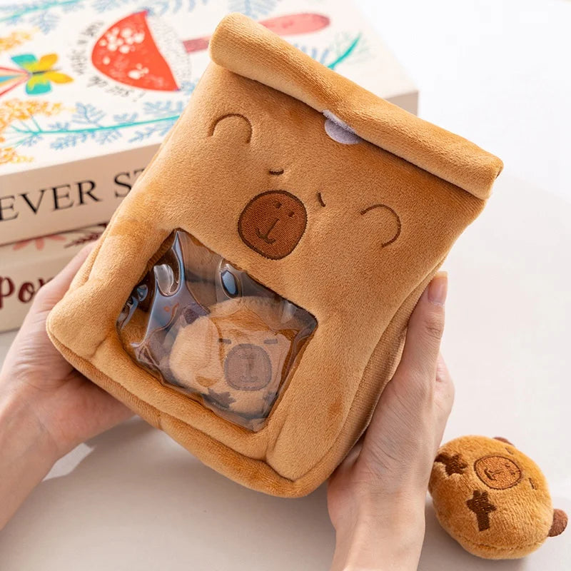 Brown kawaii plush toy with a clear window showing a smaller plush toy inside, held by a hand.