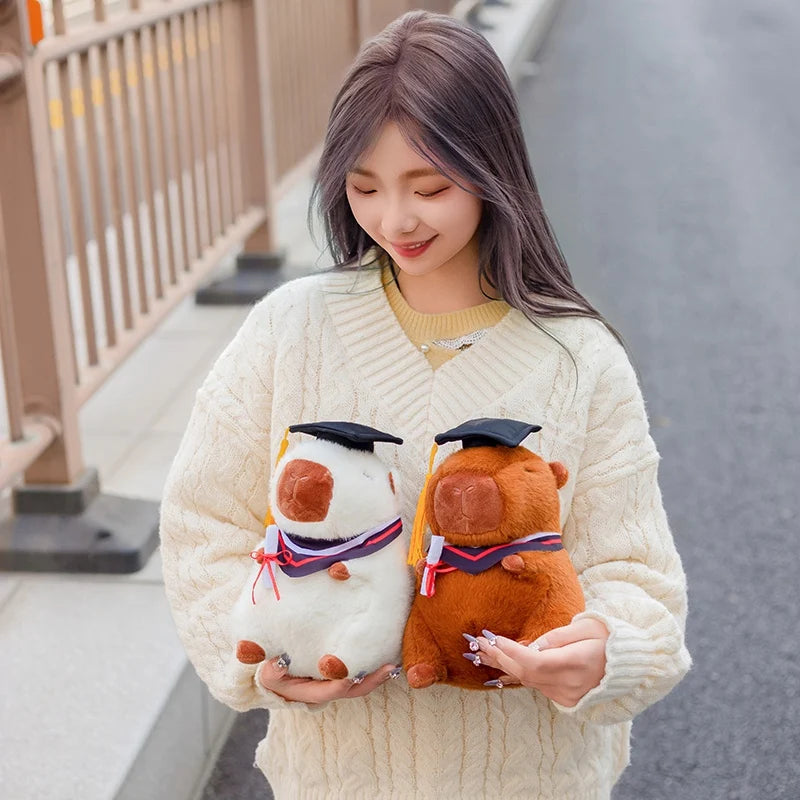 Woman holding two capybara plush toys graduation-themed animals outdoors
