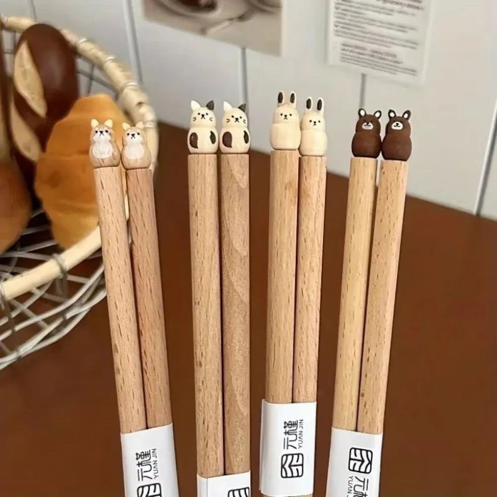 Set of wooden kawaii chopsticks with cat-shaped ends on a wooden surface.