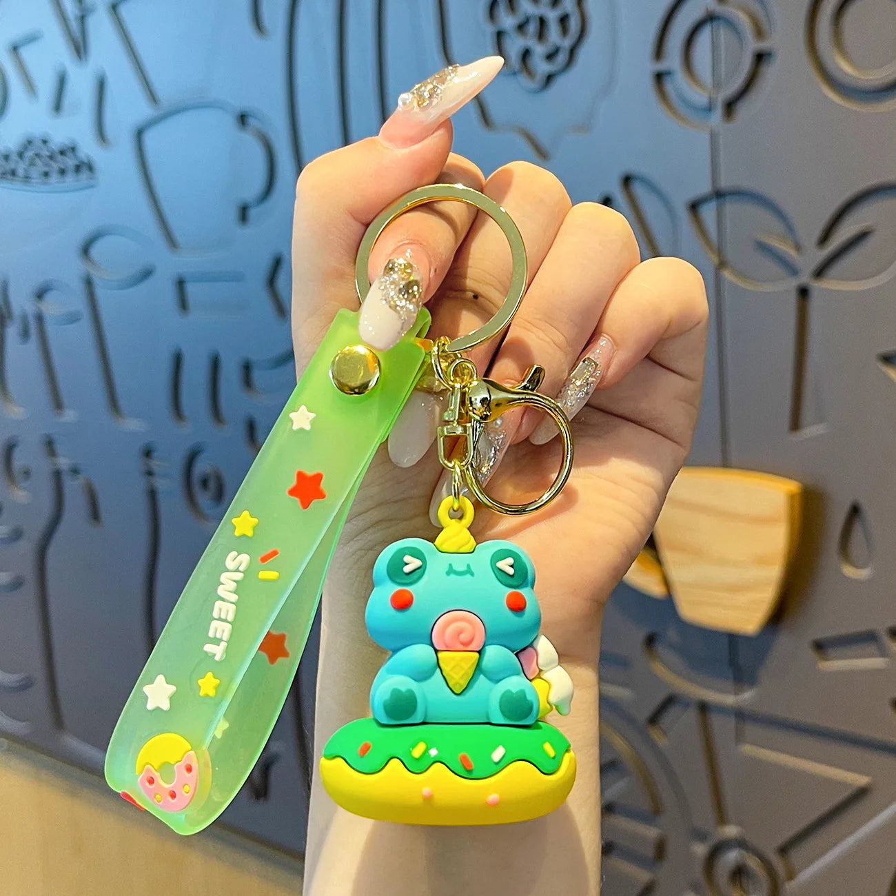 Hand holding a kawaii colorful keychain with a cartoon character against a decorative wall.