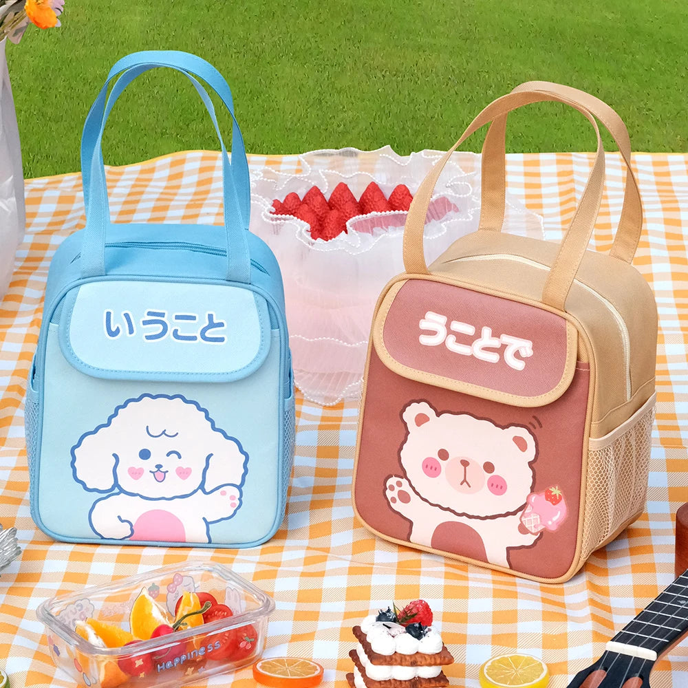 Two cartoon-themed kawaii lunch bags on a picnic blanket with fruits and a cake.