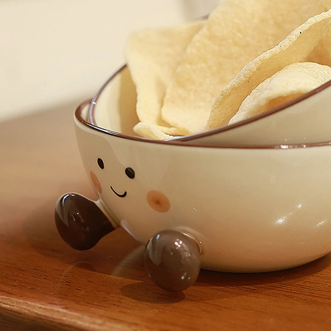 Ceramic kawaii ramen bowl with cartoon face design filled with chips on a wooden surface