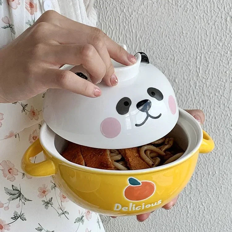 Yellow kawaii ramen bowl with a cat-shaped lid held by a person against a light-colored wall.