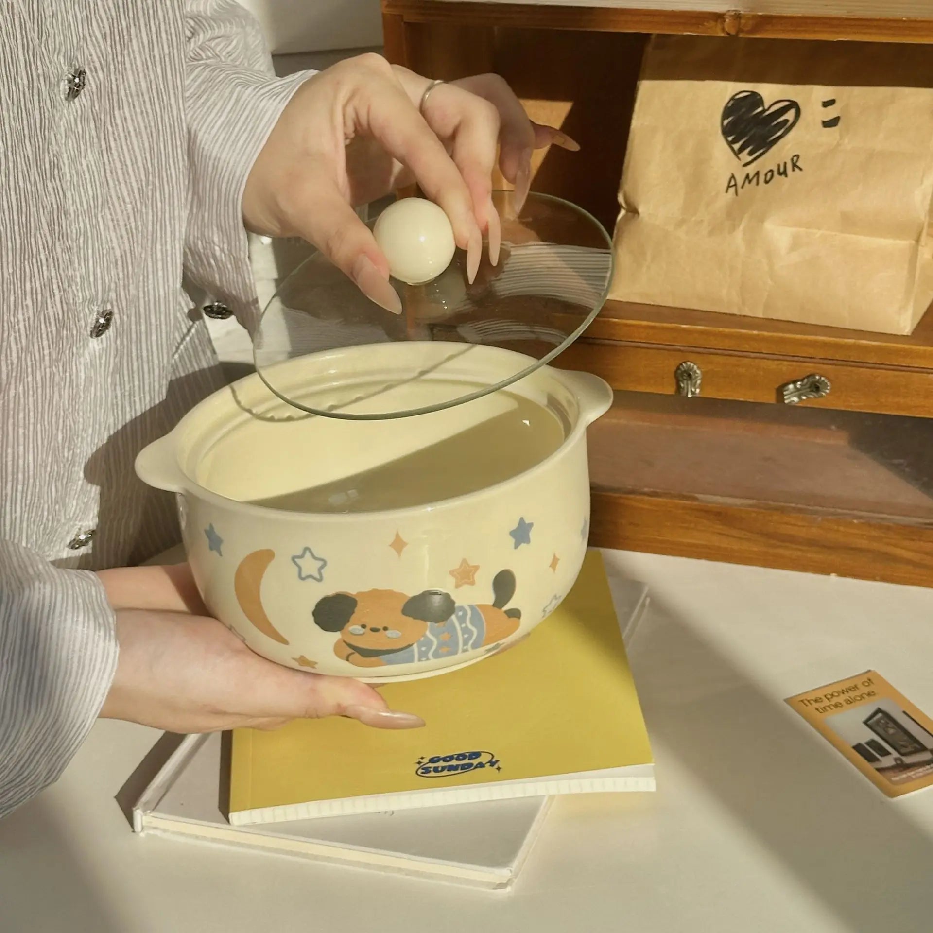 Person cracking an egg into a cartoon-patterned kawaii ramen bowl on a wooden surface.