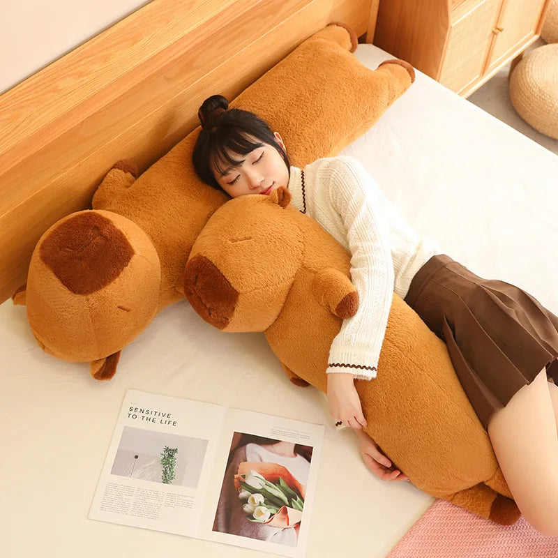 Person lying on a large brown teddy bear-shaped kawaii pillow on a bed with a magazine underneath.