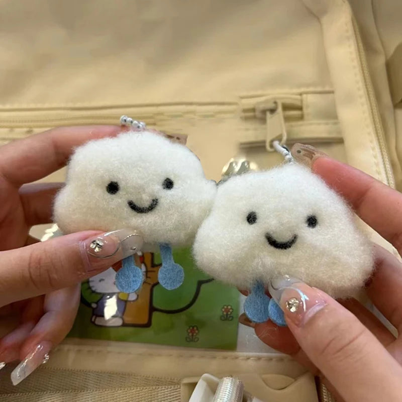 Two kawaii fluffy white keychains with smiling faces held by a person against a beige background.