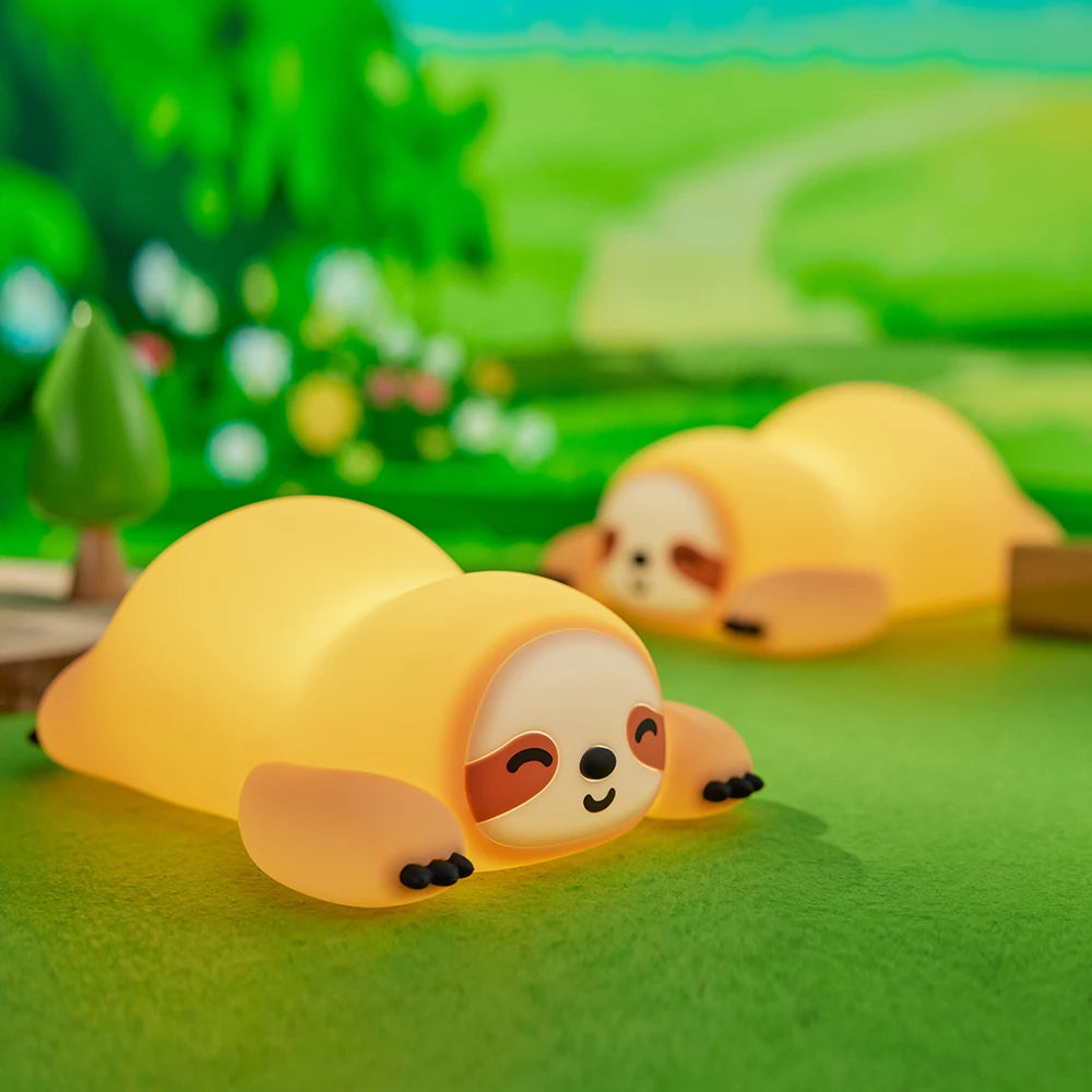 Two yellow sloth kawaii figurines on a green surface with a blurred natural background