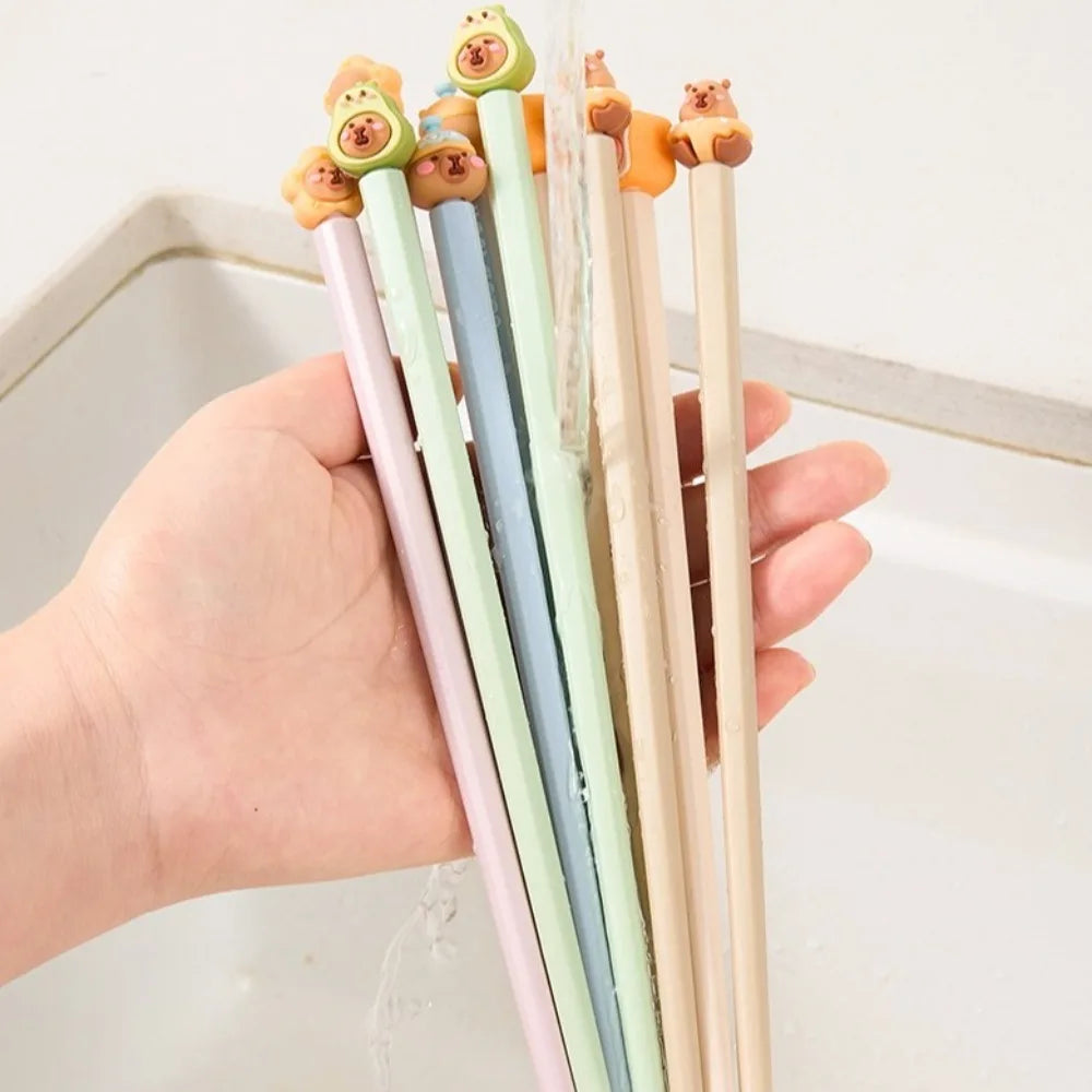 Hand holding five colorful kawaii chopsticks with cartoon animal ends on a light background