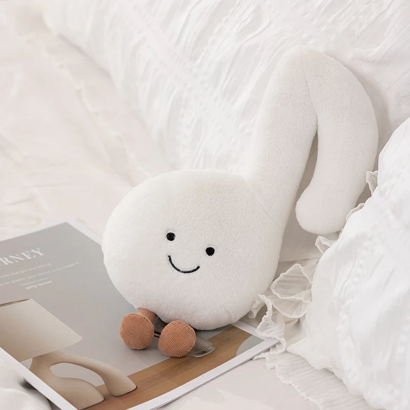 White kawaii plush toy with a smiley face on a bed with books and a lamp.
